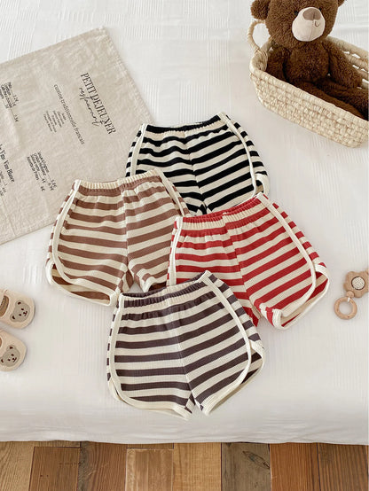 Assorted striped baby shorts in beige, brown, black, and red, laid out on a light-colored surface.
