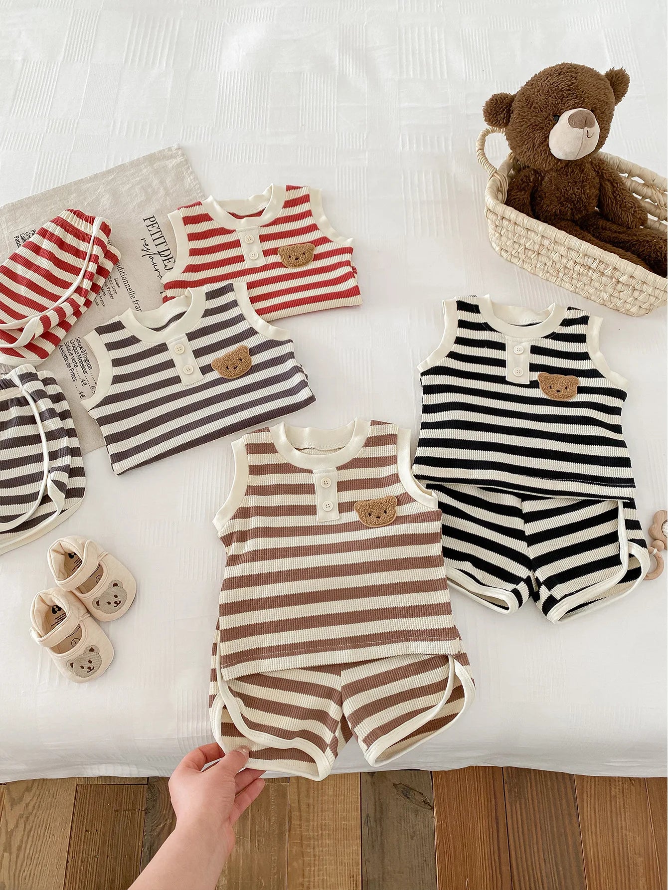 Colorful striped sleeveless baby sets in various shades, featuring bear design and shoes on a bed.