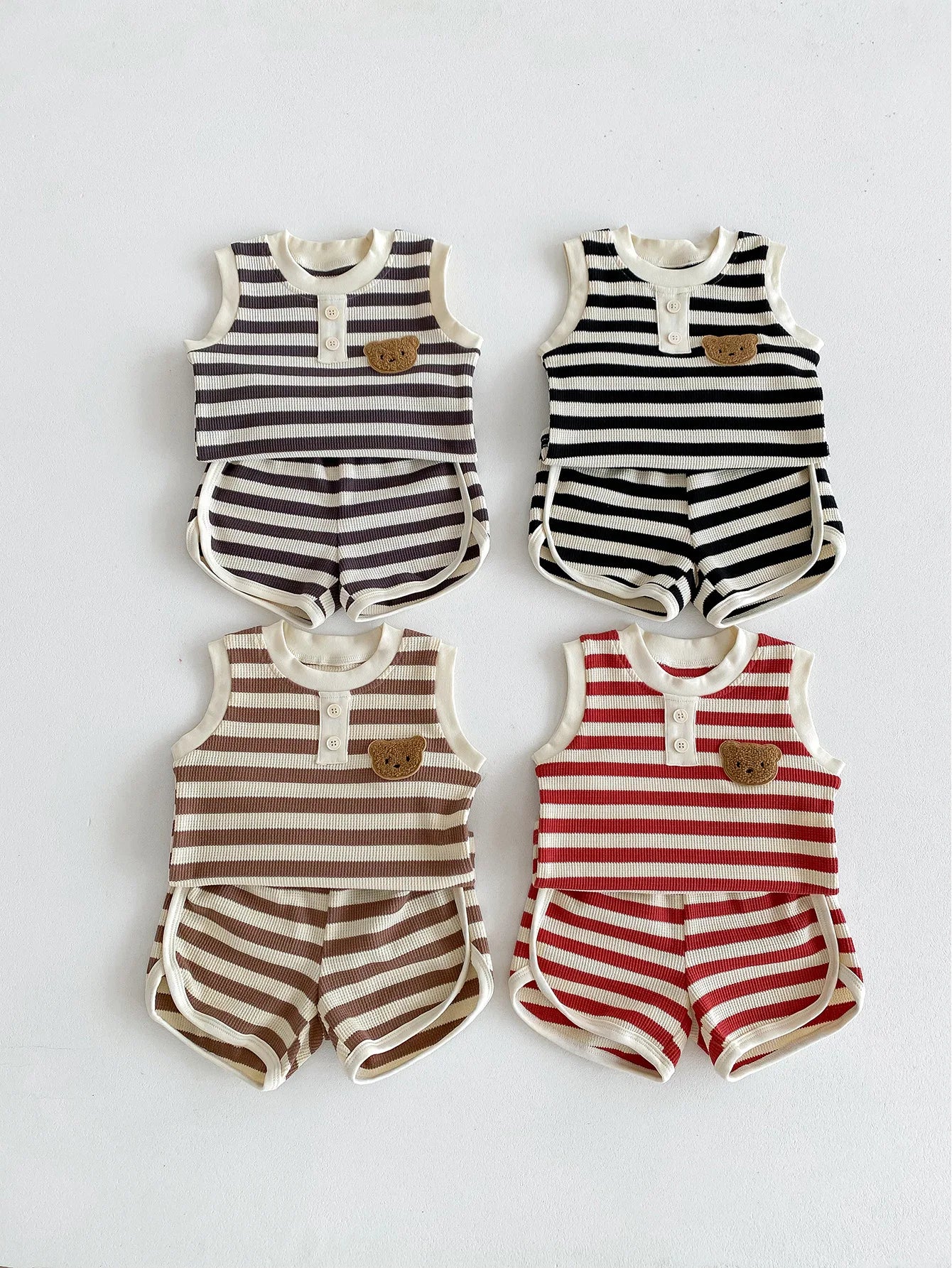 Four striped sleeveless baby sets in brown, black, white, and red, featuring shorts and bear button details.